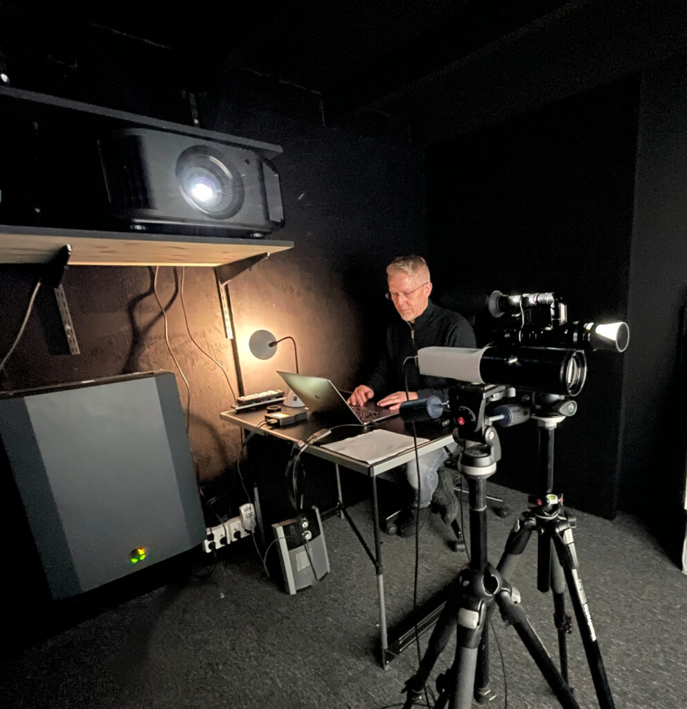 Gorm kalibrerer en JVC-projektor i AVshops kalibreringsrom med bærbar PC og profesjonelt måleutstyr. Retusjert originalfoto.